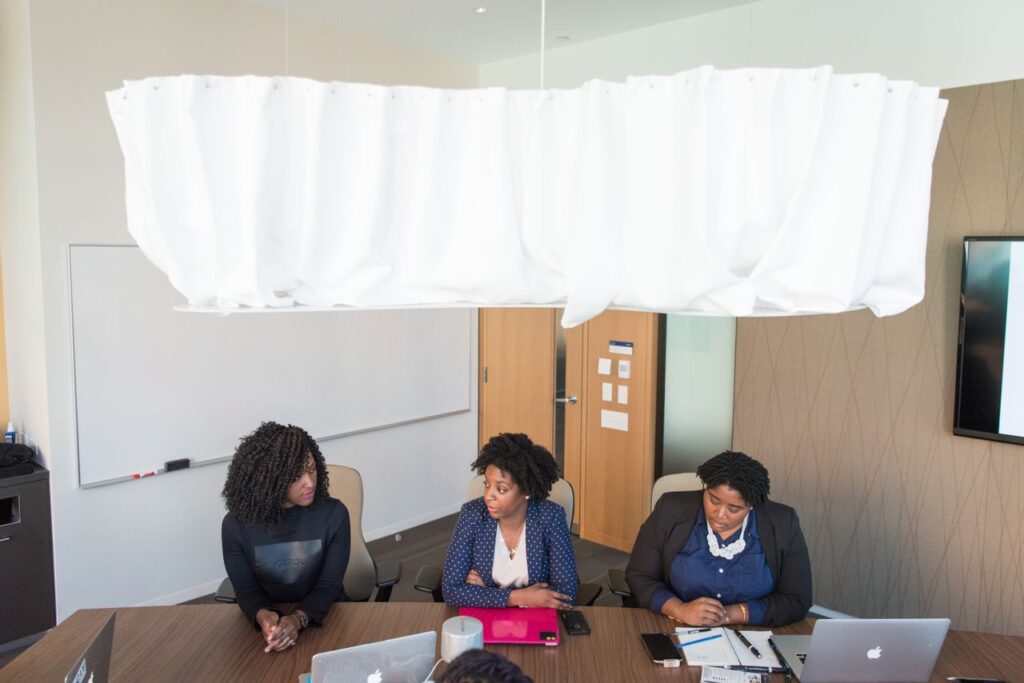 Three women in a modern office engaged in a business meeting with laptops.